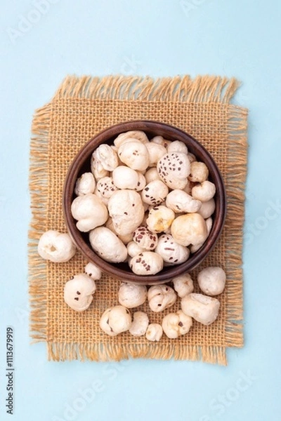 Obraz Top View of Makhana or Fox Nut in a Wooden Bowl on Burlap Fabric Isolated on Light Blue Background with Copy Space, Also Known as LEuryale Ferox, otus Seed Pop or Gorgon Nut