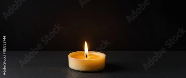Fototapeta A warm candle glowing softly on a black background, ideal for relaxation and ambiance