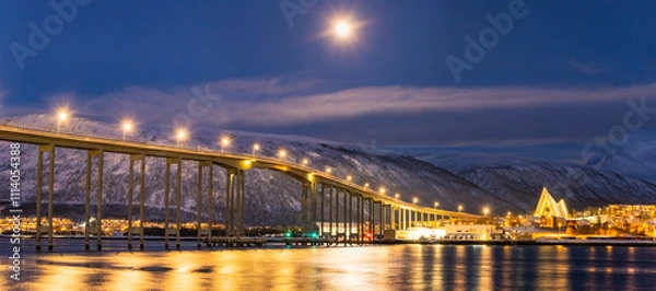 Fototapeta Panorama of the Norwegian city of Tromso on a winter evening during the Christmas season. The bridge over the fjord and houses are illuminated by city lights