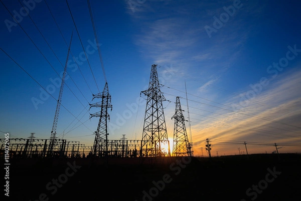 Fototapeta Many high-voltage power towers, silhouetted against the setting sun