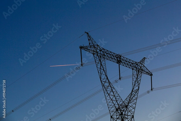 Fototapeta Many high-voltage power towers, silhouetted against the setting sun