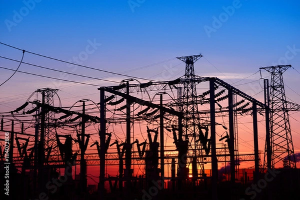 Fototapeta Many high-voltage power towers, silhouetted against the setting sun