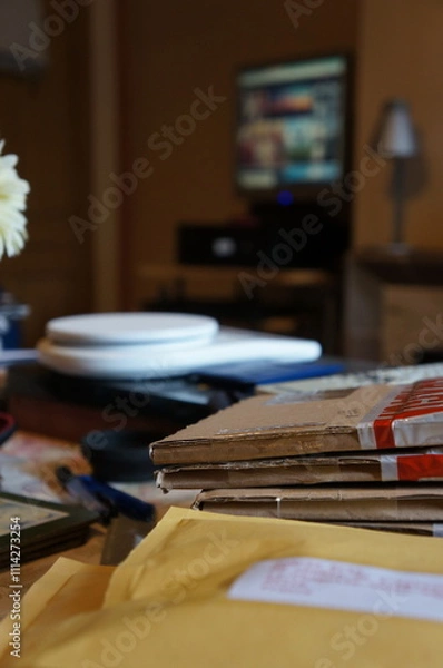Fototapeta Envelopes and parcels with soft-focused weighing scales and a computer in the background at home.