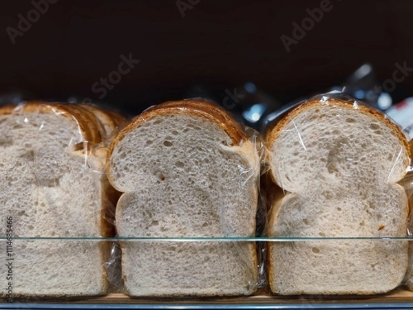 Fototapeta Unbranded slices of white bread wrapped in plastic are on a supermarket shelf ready to be sold in the shop at the bakery section