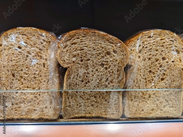 Fototapeta Unbranded slices of brown bread wrapped in plastic are on a supermarket shelf ready to be sold in the shop at the bakery section
