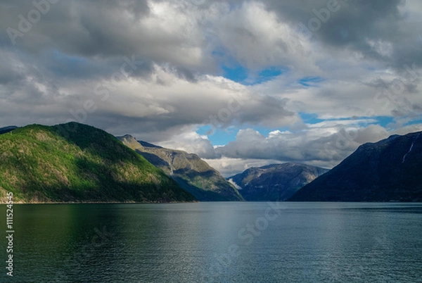 Fototapeta Cloudy sky over banks of fjord. Mountains with green forest, Eidfjord, Norway