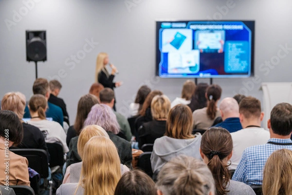 Obraz Diverse audience attentively listening to a speaker at a business conference. Presentation displayed on a big screen in a modern meeting room setting.