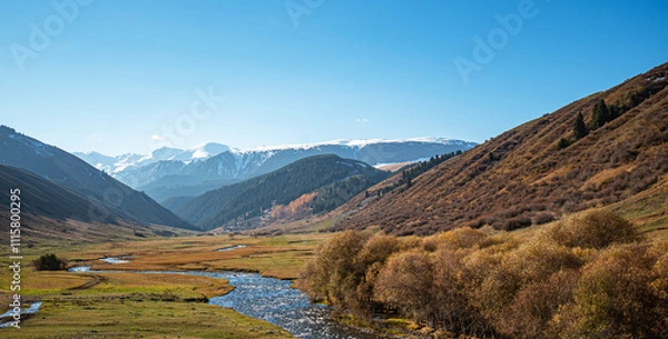 Fototapeta Mountains river winding through a mountainous valley with autumn shrubbery and distant snow-covered peaks under a bright blue sky.