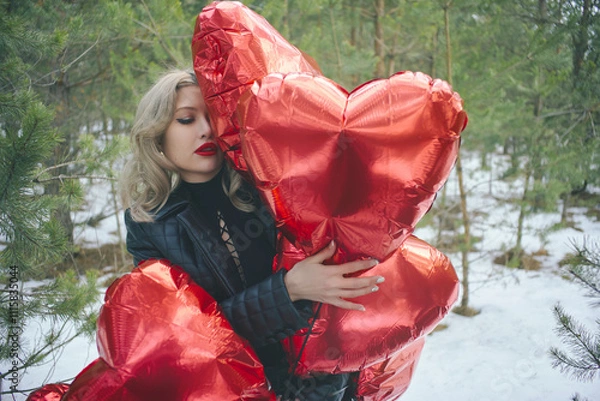 Fototapeta portrait of a young woman hugging red balloons in the shape of hearts . The girl with bright makeup and red lipstick holds the balloons to herself, creating an atmosphere of romance and tenderness.