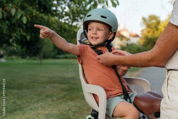 Obraz A smiling child being secured in a bicycle seat by a parent, ready for a safe outdoor ride and adventures.