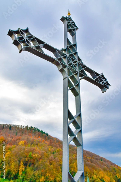 Fototapeta An imposing large metal cross stands majestically in front of a mountain