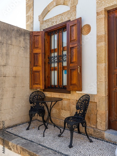 Fototapeta Tisch mit zwei Stühlen vor einem Fenster mit Holzladen auf Rhodos