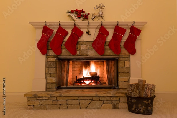 Fototapeta Six red Christmas stockings adorn a stone fireplace with a cozy fire.