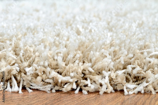 Fototapeta Close-up of white shaggy carpet on brown wooden floor