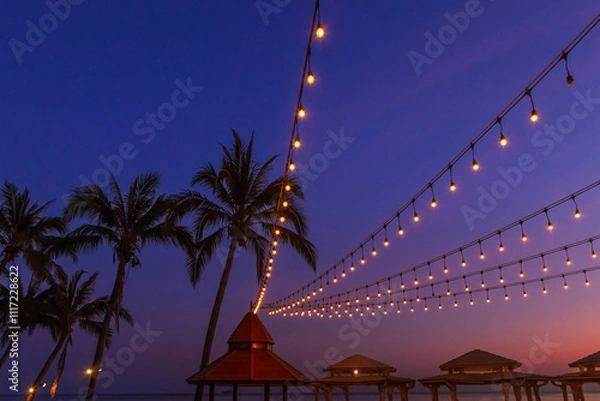 Obraz Atmosphere view sunset bars with light bulbs hanging on silhouette coconut palm trees on the beach