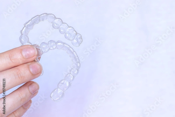 Fototapeta Hand holding Invisalign transparent braces on white background with copy space. Invisible retainers and aligners