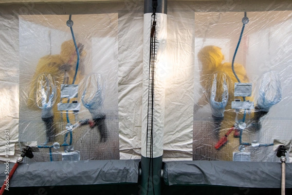Fototapeta Firefighters in protective hazmat suits in a decontamination shower