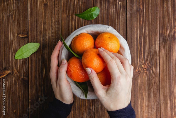 Obraz Tangerines in a straw basket on a brown wooden table.