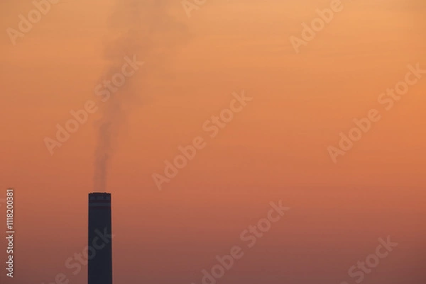 Fototapeta Close up with copy space of smokestack emits pollution into a hazy orange sky, symbolizing industrial impact and environmental challenges like air quality, global warming and climate change.