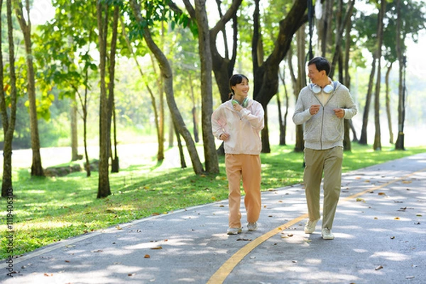 Fototapeta Cheerful middle aged man and his daughter enjoying a light jogging or brisk walking session on park trail