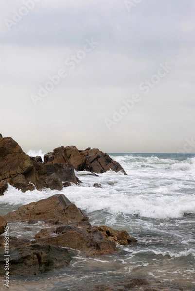 Fototapeta Stormy Ocean Waves Crashing Against Rocks with a Lighthouse in the Background