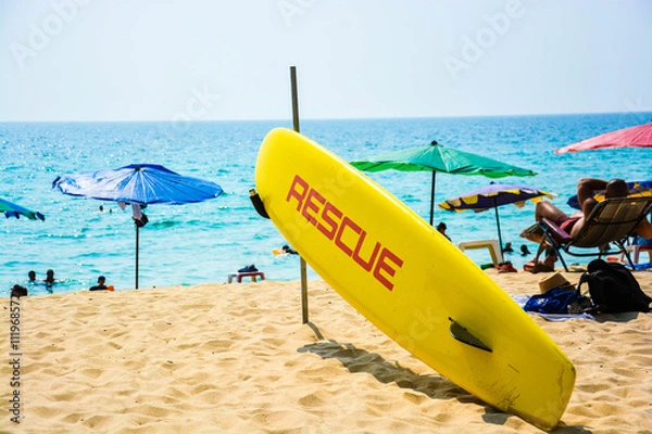 Obraz A rescue surf board standing on a beach in Phuket, Thailand with lots of tourists.