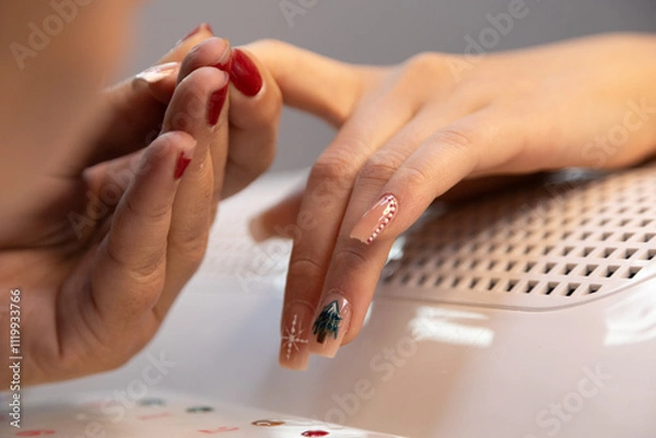 Obraz A professional nail technician makes Christmas nail designs in a beauty salon. Woman hands with Christmas tree and candy cane design. Merry Christmas. Candy cane nails. Snowflake nails. Winter nails.