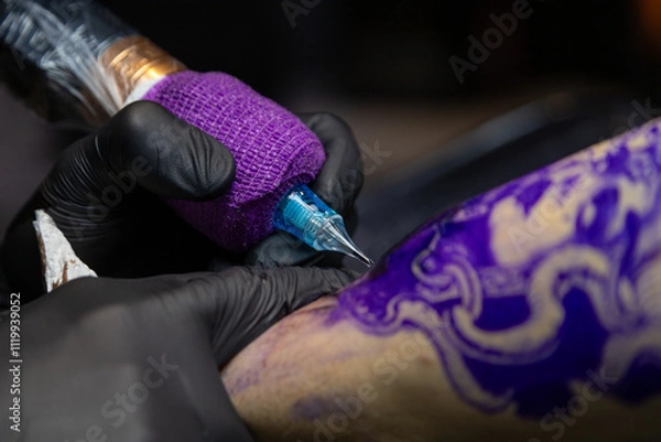 Obraz Close-up shot of a tattoo artist using a tattoo machine to create a detailed design on a client’s arm, with a focus on the purple stencil and black gloves. Perfect for tattoo art, creativity, and life