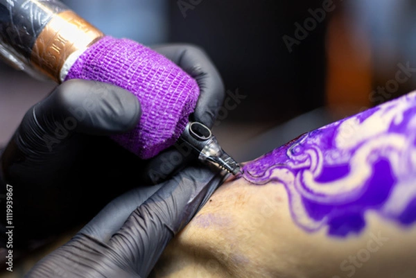 Obraz Close-up shot of a tattoo artist using a tattoo machine to create a detailed design on a client’s arm, with a focus on the purple stencil and black gloves. Perfect for tattoo art, creativity, and life