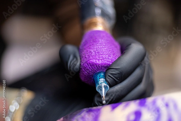 Obraz Close-up shot of a tattoo artist using a tattoo machine to create a detailed design on a client’s arm, with a focus on the purple stencil and black gloves. Perfect for tattoo art, creativity, and life