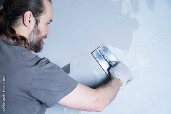 Obraz A person smoothly spreads epoxy adhesive or decorative plaster on a wall using a trowel in a workshop setting.