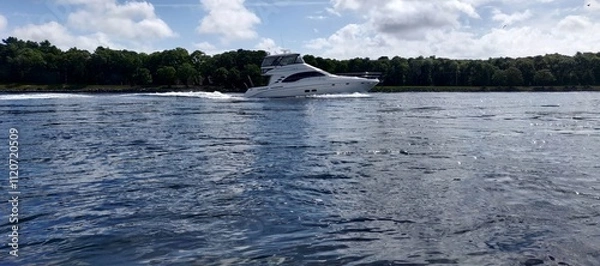 Fototapeta A boat is in the water with a small wave behind it