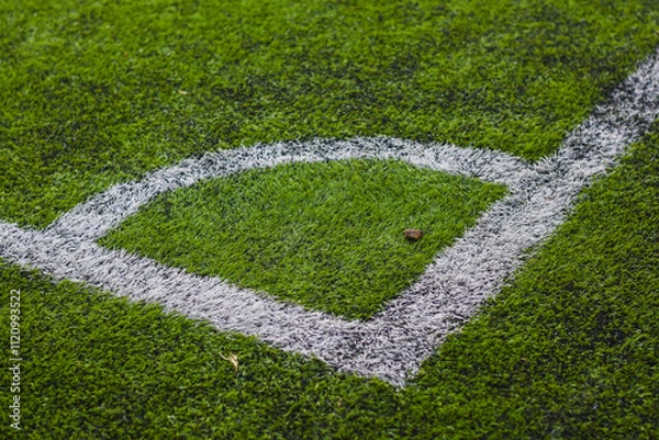 Fototapeta close-up view of a section of a sports field, specifically a corner area. The field is covered in green artificial turf with white painted lines marking the boundaries.
