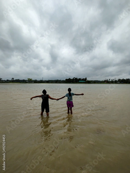 Obraz Silhouette of Two People Walking in Flooded Water Under Dramatic Cloudy Sky