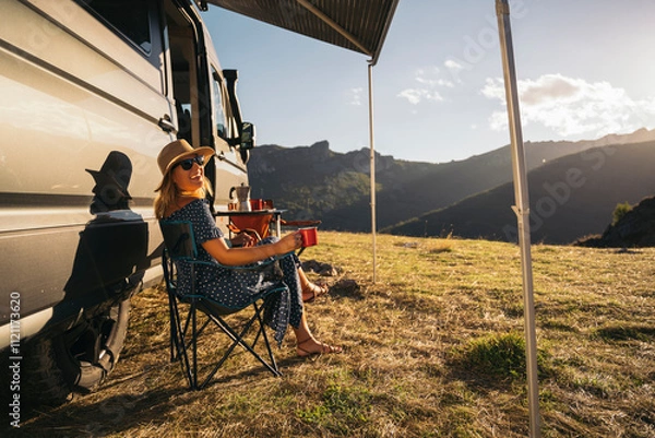 Obraz A woman relaxes by a camper van, enjoying a remote retreat with picturesque mountain scenery