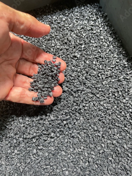 Obraz plastic raw material, hand holding a handful of black plastic pellets on a gray plastic drawer, production of plastic parts, plastic injection, spilling of plastic grains with glass fiber