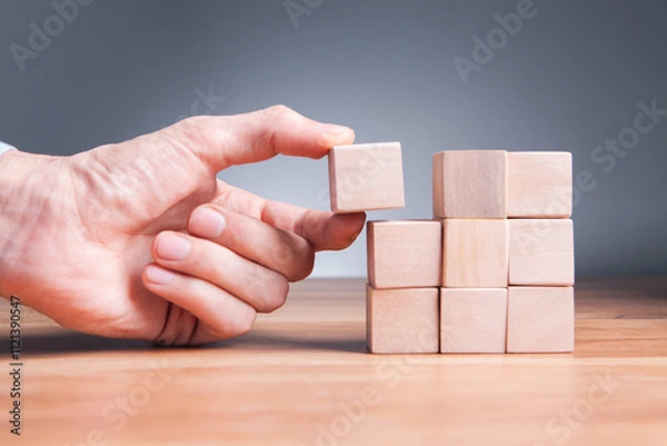 Fototapeta man hand holding wooden block with wooden blocks on white background, business and success concept.