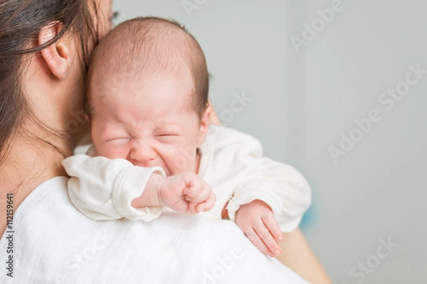 Obraz Newborn baby screaming in pain with colic on mother's shoulders
