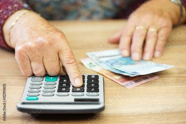 Fototapeta Older woman is using calculator to calculate all expenses