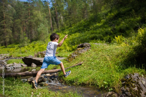 Fototapeta Little boy jumps over a stream in a forest