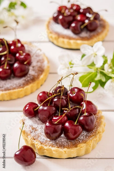 Fototapeta Tarts with almond stuffing and sweet cherry on a white wooden background with flowering branches of apple trees 