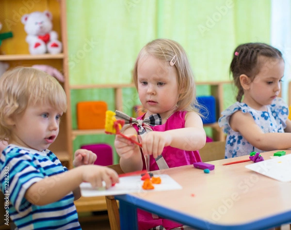 Fototapeta Kids or children creating arts and crafts in kindergarten. Girl is communicating with boy.