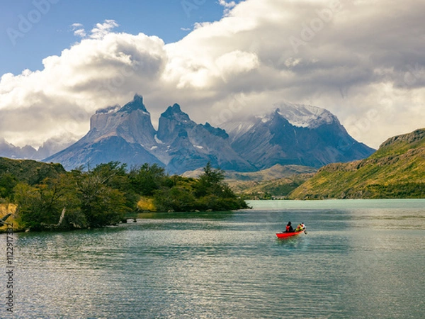 Fototapeta A vibrant red canoe glides across turquoise waters in Chilean Patagonia, surrounded by rugged mountains, lush greenery, and dramatic clouds in Torres del Paine.