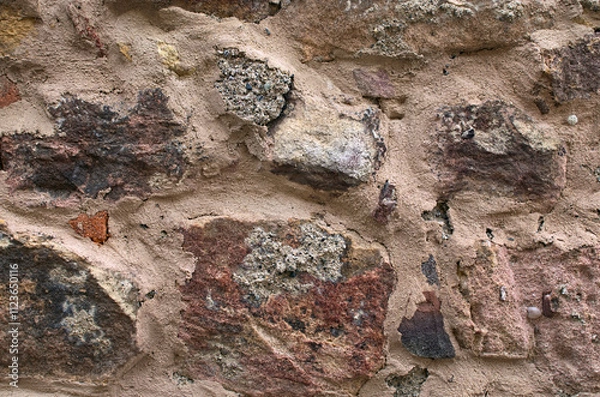 Fototapeta Detailed view of an ancient handcrafted stone wall. The multi-colored exposed stone, brick and mineral layer. Stone pattern, geological texture. Bright red-brown stone background. Abstract background