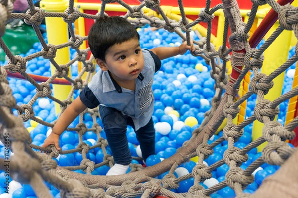 Fototapeta little boy playing inside a tunnel in the playground balls poll