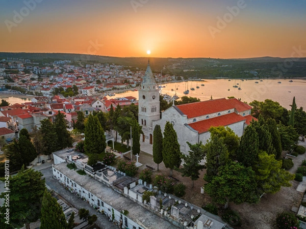 Fototapeta Primosten, Croatia - Aerial view of St. George's Church on Primosten peninsula and old town on a sunny summer morning in Dalmatia, Croatia. Golden sky at sunrise by the Adriatic sea coast