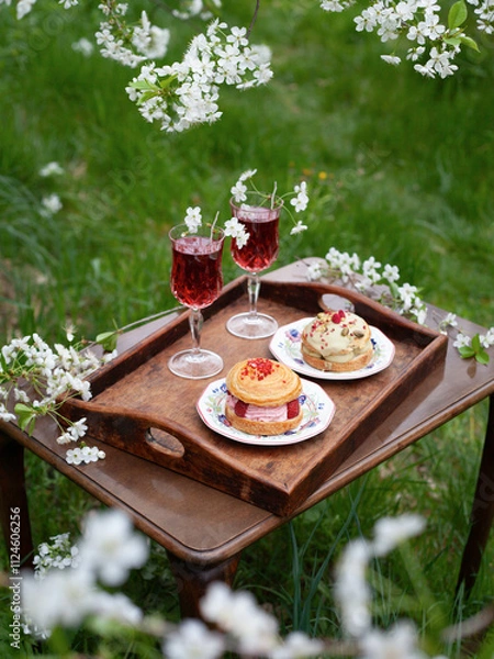 Fototapeta Spring picnic in blooming apple orchard -  vintage table cherry cocktails and sweet cakes are perfect setting for a romantic date.