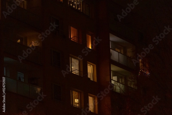 Fototapeta A tall building featuring numerous windows is beautifully lit up at night, casting a warm glow against the surrounding darkness of the evening sky