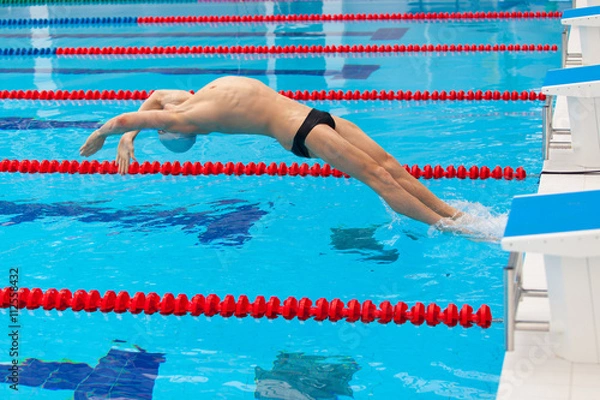 Fototapeta Young muscular swimmer jumping from starting block in a swimming pool