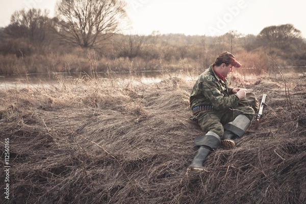 Fototapeta Hunter preparing for hunting in morinig field nearby river during sunrise